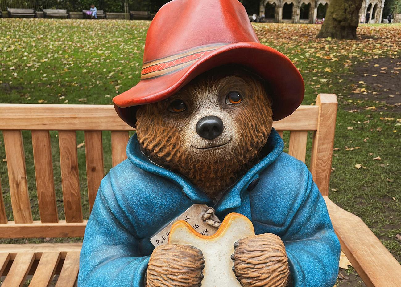 Paddington Bear sat on a park bench eating a marmalade sandwich