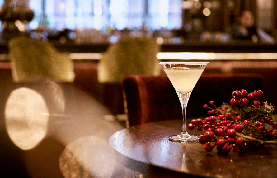 Cocktail glass on a wooden table with festive red berries and greenery in an upscale bar setting