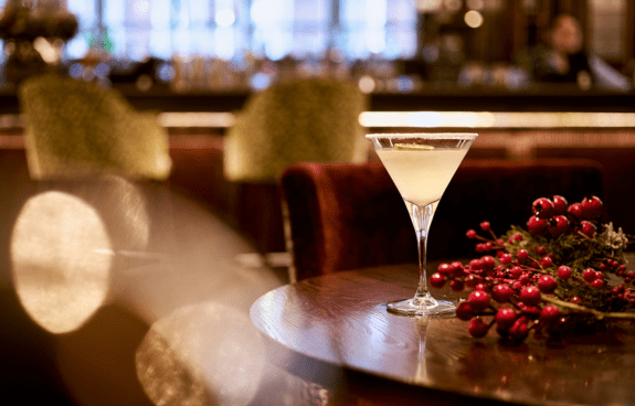 Cocktail glass on a wooden table with festive red berries and greenery in an upscale bar setting