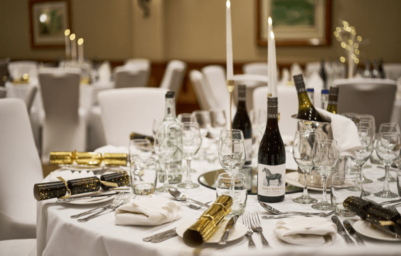 Formal dining table with white linens, candles, wine bottles, and glassware set for an event