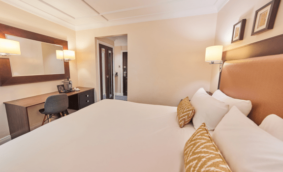 Deluxe King bedroom with desk, mirror, and doorway to ensuite bathroom.