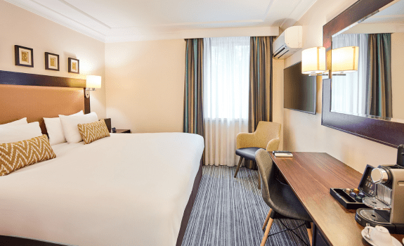 Heathrow hotel room with a large bed, desk, chair, and coffee machine