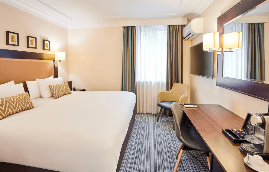 Heathrow hotel room with a large bed, desk, chair, and coffee machine