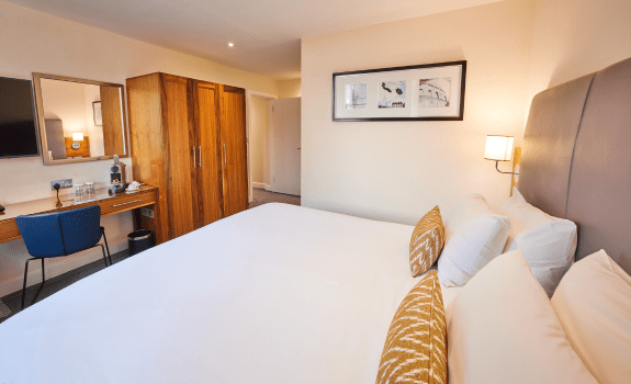 Executive King bedroom with large bed, wooden wardrobe, desk, and wall art.