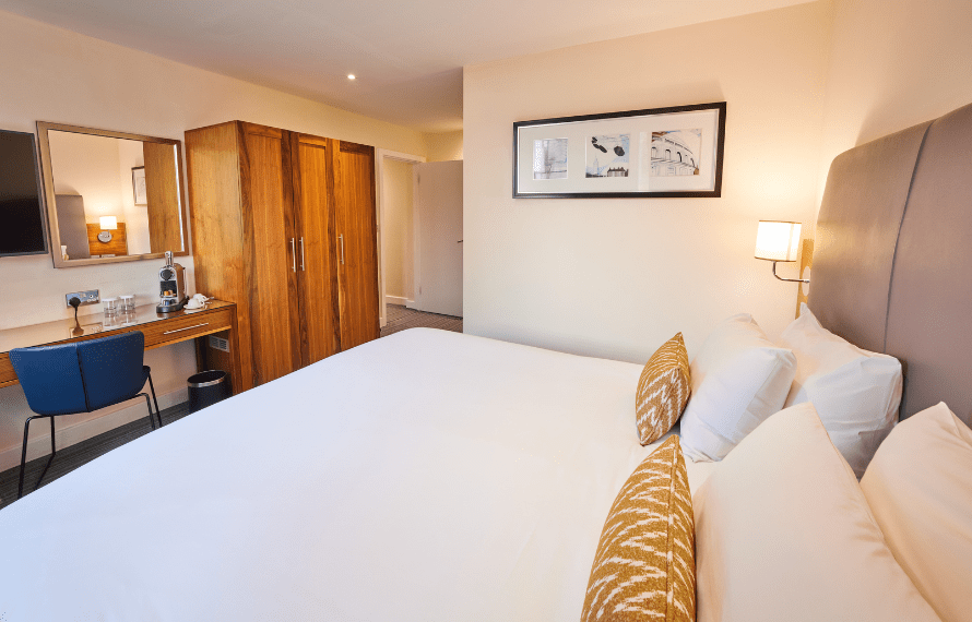 Executive King bedroom with large bed, wooden wardrobe, desk, and wall art.