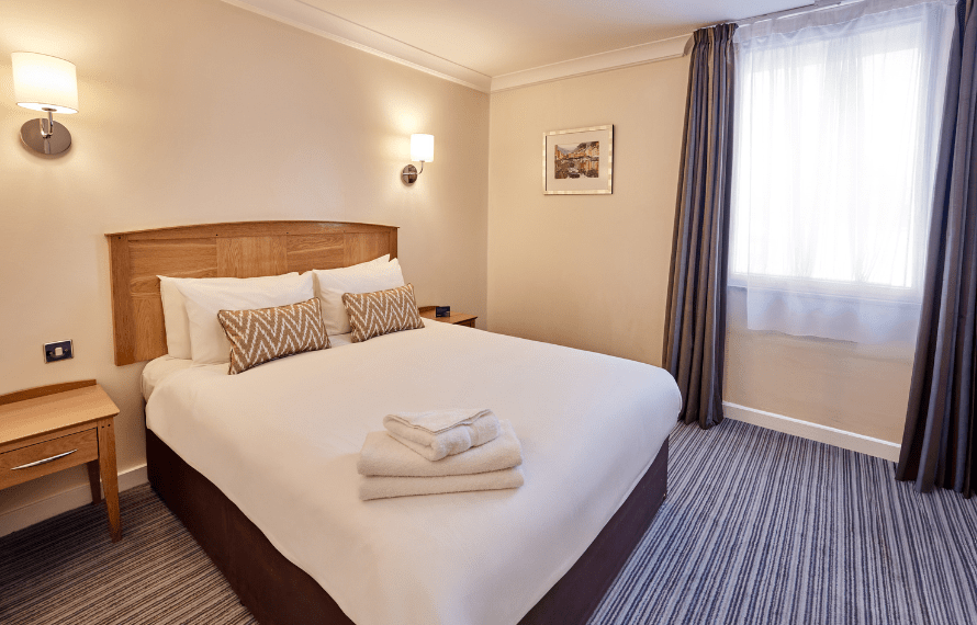 Bright Standard Double bedroom with bed, bedside tables, and folded towels.