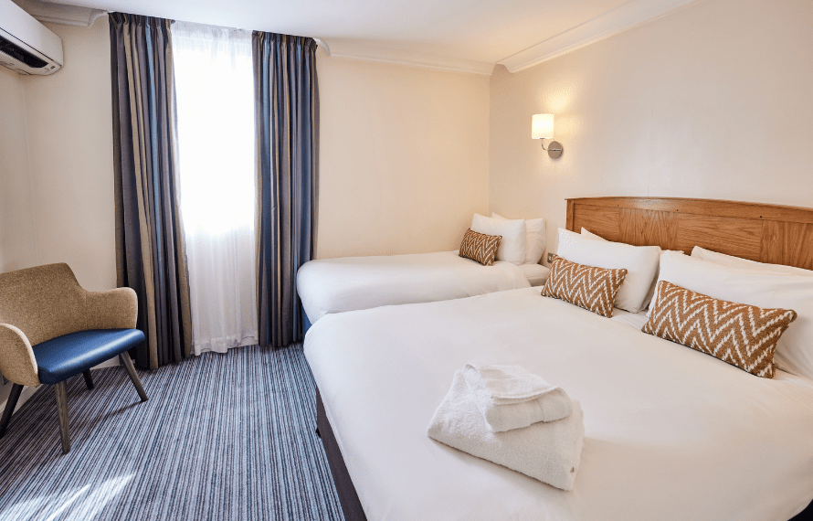 Spacious family bedroom with double and single beds, striped carpet, and bedside lamps.