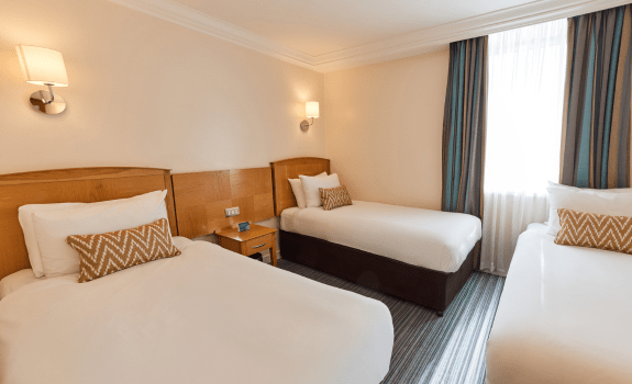 Standard Family bedroom with three single beds, bedside table, and window with curtains.