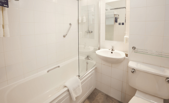 Bathroom with bathtub, overhead shower, and white tiled walls.