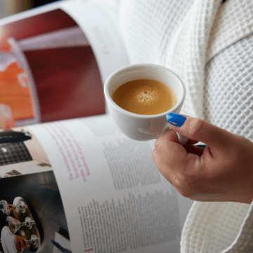 Photo of hand holding espresso mug whilst reading magazine