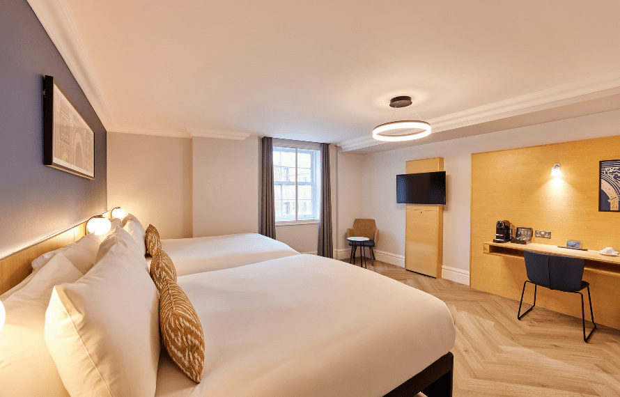 Deluxe family room at Thistle Park Lane with two beds, wall‑mounted TV, work desk with coffee facilities, and wooden flooring.