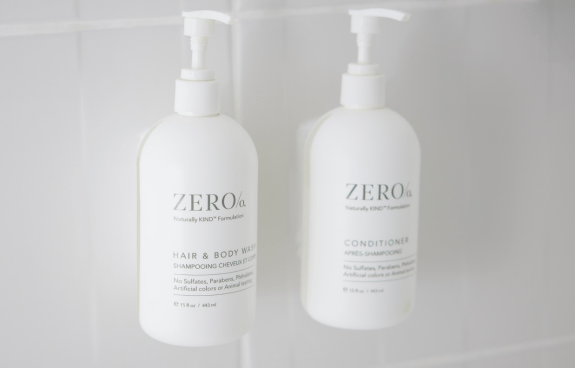 Wall‑mounted Zero% branded hair and body wash and conditioner bottles in a hotel shower.