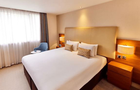 Deluxe king room with a large bed, white bedding, nightstands, and an armchair by the window