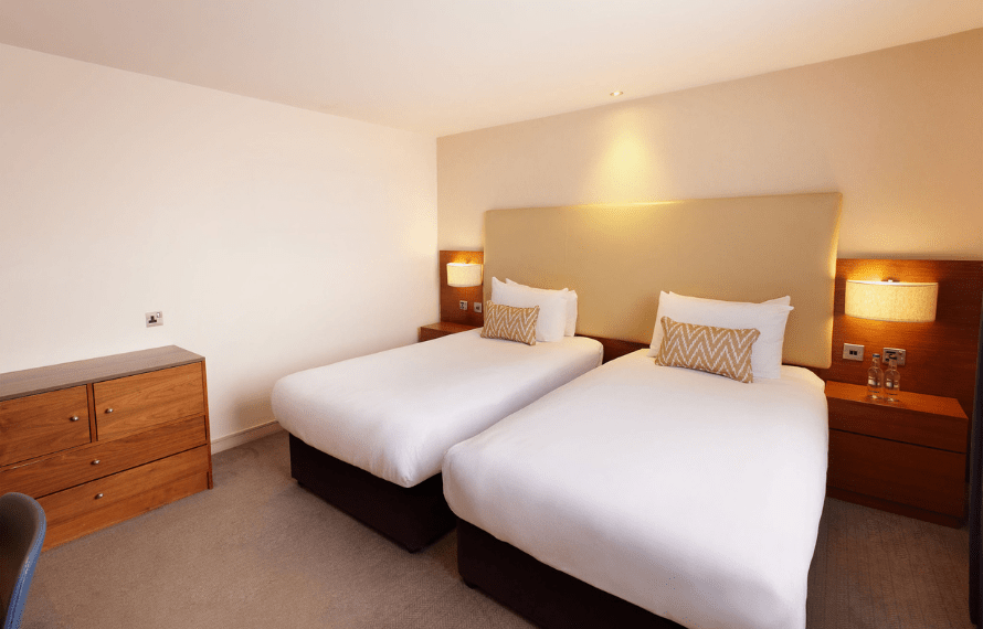 Hotel room with two single beds, geometric-patterned pillows, nightstands, and a wooden dresser
