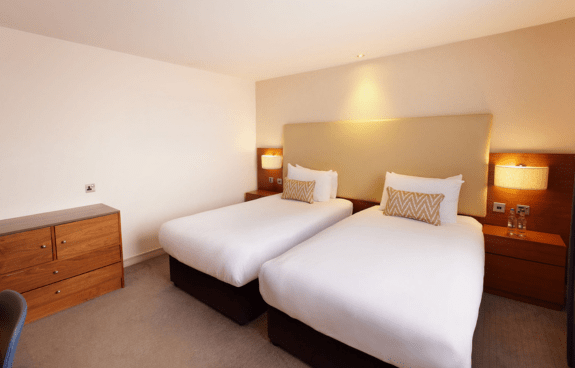 Hotel room with two single beds, geometric-patterned pillows, nightstands, and a wooden dresser
