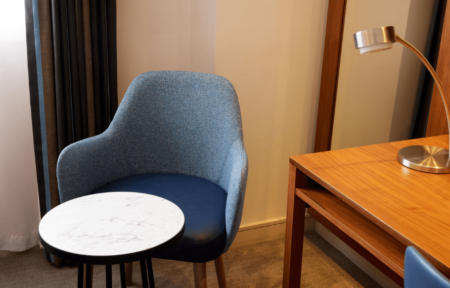 Room corner with a blue chair, marble-top side table, and wooden desk with a metallic lamp
