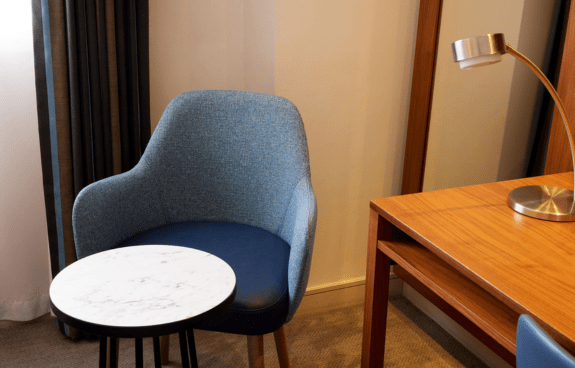 Room corner with a blue chair, marble-top side table, and wooden desk with a metallic lamp